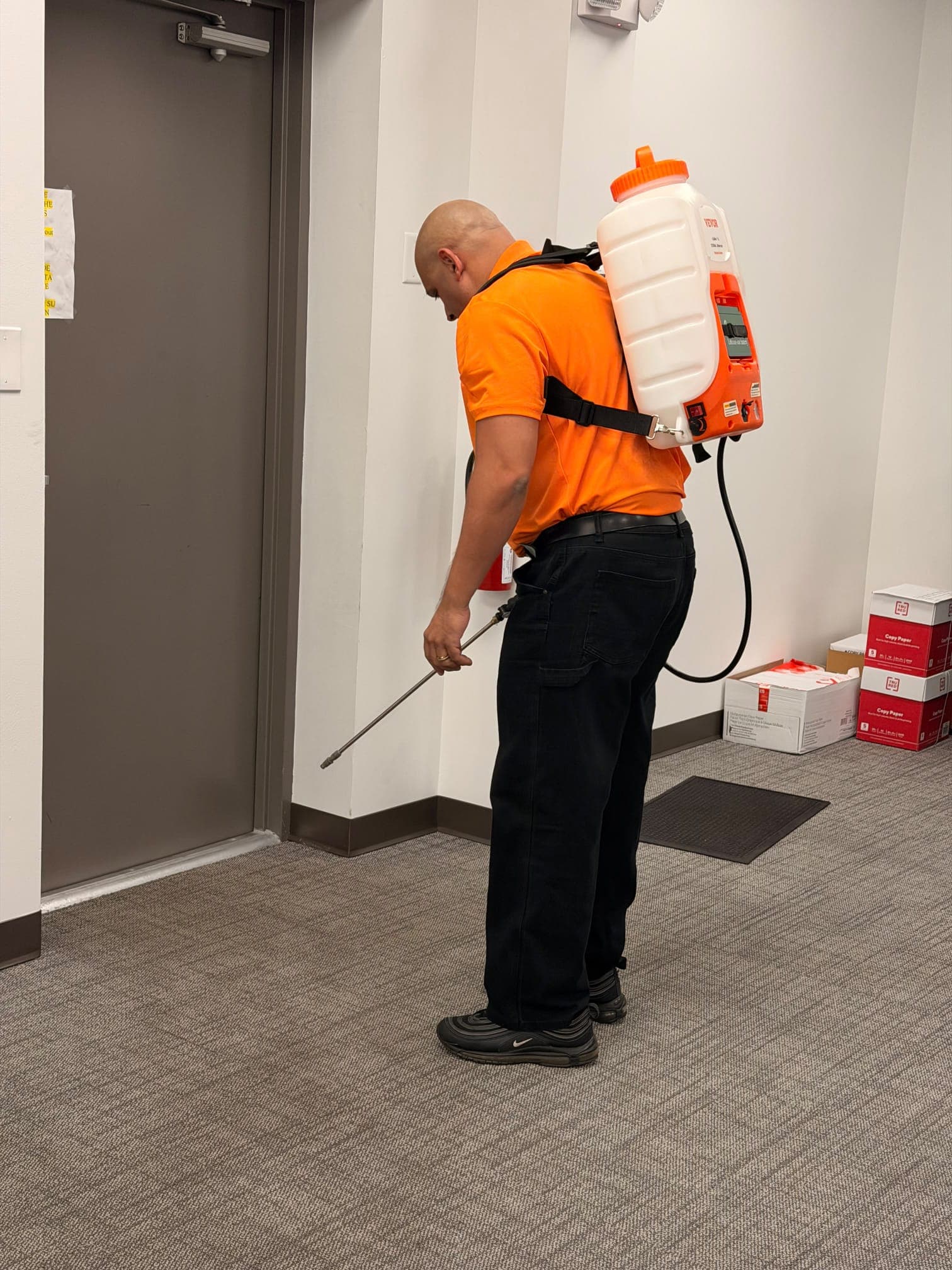An INGAL SERVICES INC employee applying disinfectant with a backpack sprayer along a client corridor