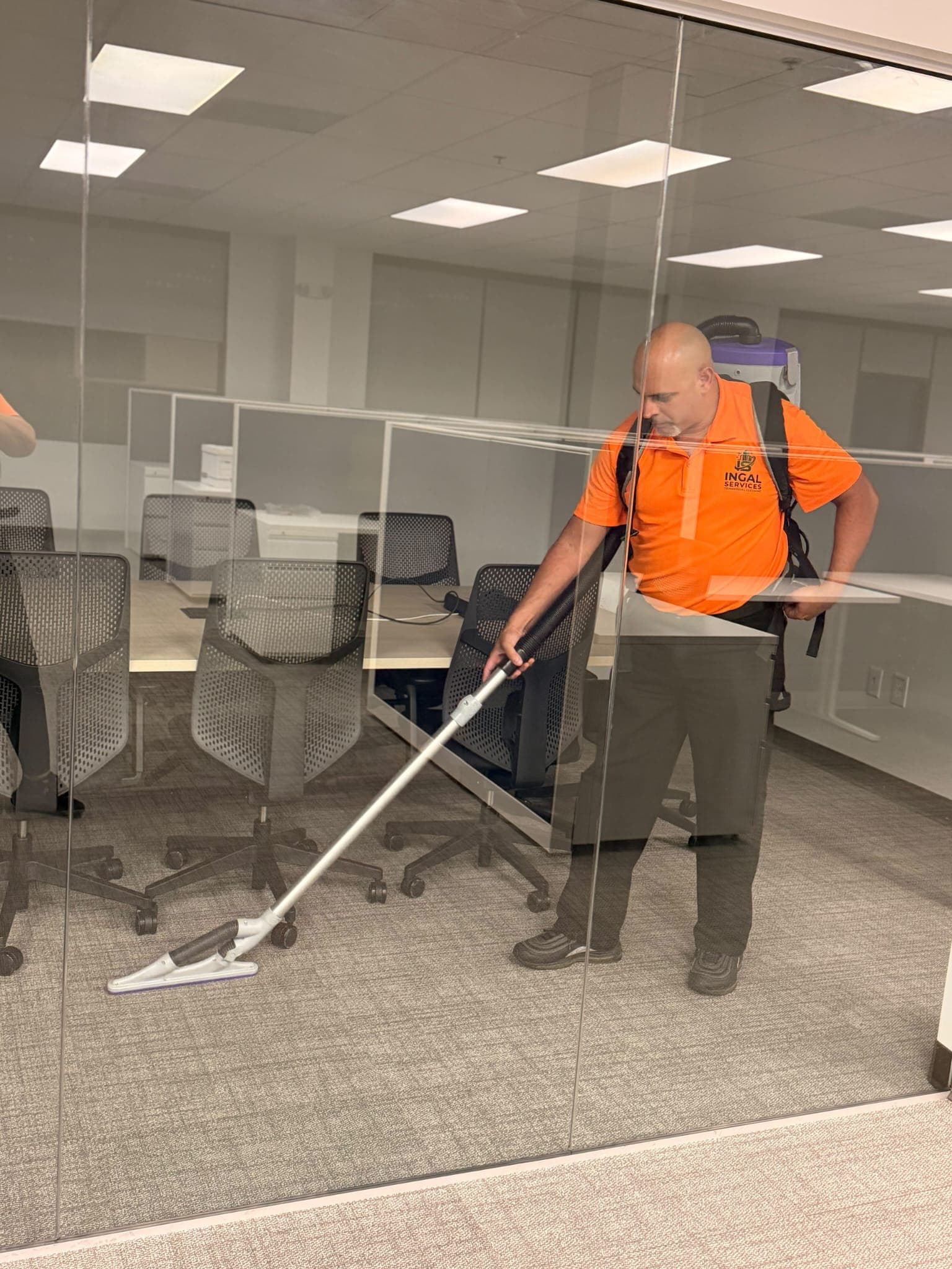 INGAL SERVICES INC employee dust mopping an open plan office floor seen through a glass partition