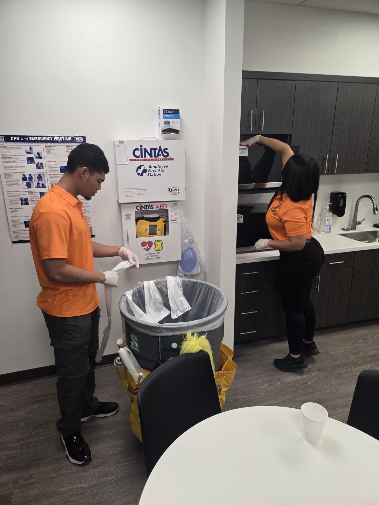 Two INGAL SERVICES INC employees servicing a breakroom together, one lining a barrel and one wiping the microwave