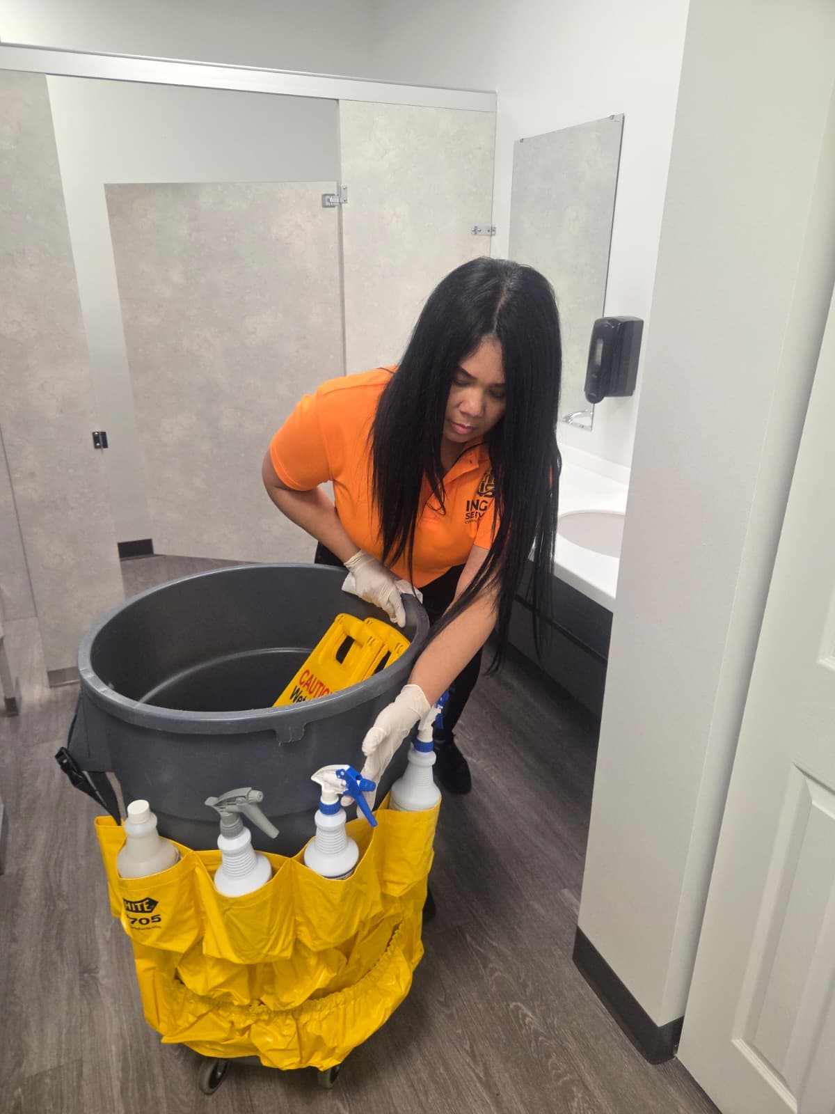 INGAL SERVICES INC employee restocking a janitorial cart inside a commercial restroom